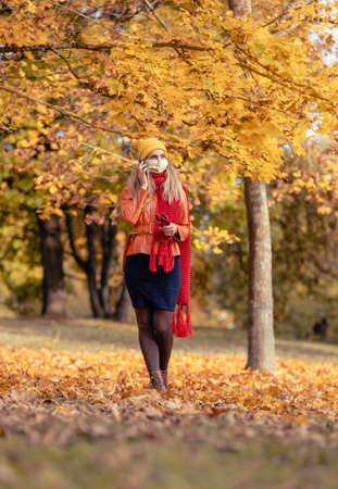 Woman using her phone having walk in fall park during coronavirus crisis amidst colorful foliageの写真素材