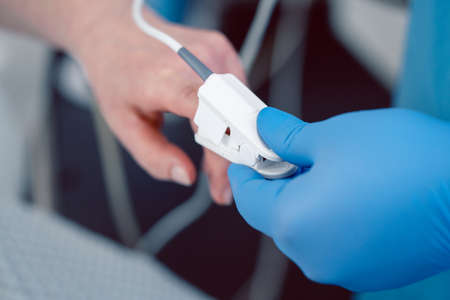 Nurse in hospital putting blood pressure sensor on patients finger to prepare for surgeryの写真素材