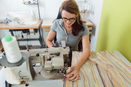 Seamstress sews colorful decorative fabric on sewing machine in a tailors shopの写真素材
