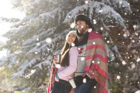 Young couple posing in snowfall with coffee cup