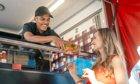 Friendly Cook in a food truck handing tasty burger over to woman customerの写真素材