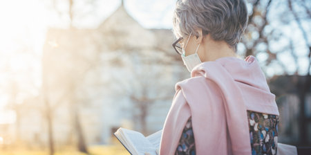 Senior lady praying with face mask reading the bible in front of a church in Covid-19 timesの写真素材