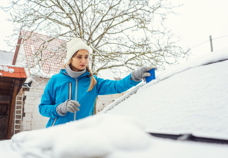 Woman scraping off ice from front window of her car in winter being a bit annoyedの写真素材