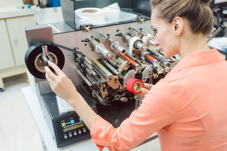 Diligent worker woman putting new labels in printing machineの写真素材