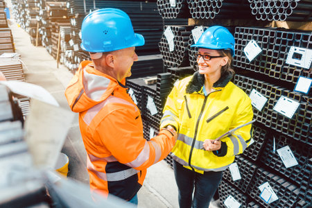 Customer and worker in steel delivery warehouse shaking hands to find an agreement