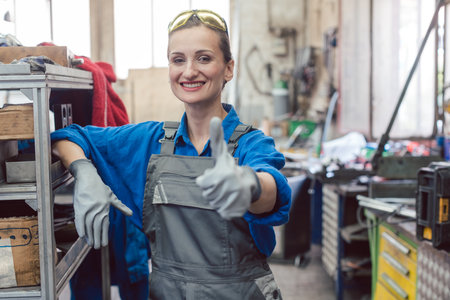 Woman worker in metal workshop showing thumbs-up into camera