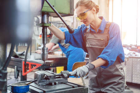 Metal worker woman operating drilling machine concentrating on her job