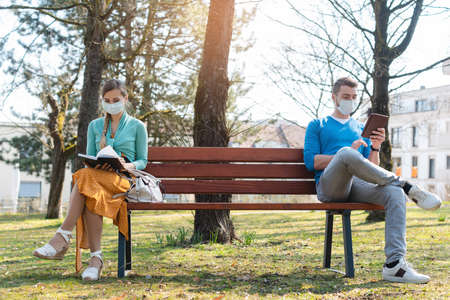 Woman and man in social distancing sitting on bench in parkの写真素材