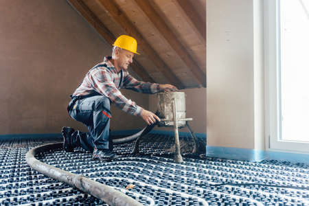 Worker on construction site installing pipes for underfloor heating system kneeling on the floorの写真素材