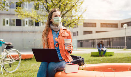 Student learning on university campus during lockdown sitting in front on main buildingの写真素材
