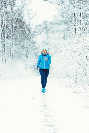 Woman jogging towards camera in cold and snowy forest for fitness gainsの写真素材