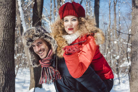 Man carrying his wife piggyback in winter while she is blowing a kiss at the cameraの写真素材