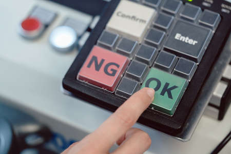Factory worker pressing the OK button on a machine to start productionの写真素材