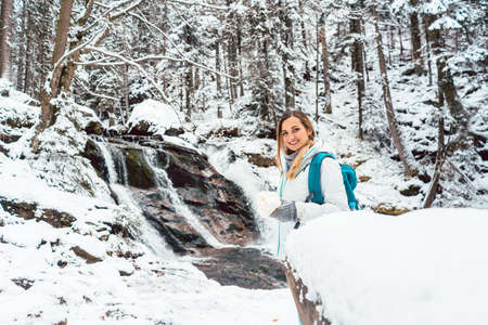 Beautiful hiker woman in front of small waterfall in the woods during winterの写真素材
