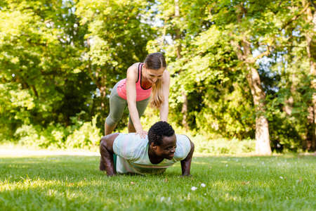 Mixed race couple doing fitness pushups in the park on summer meadowの写真素材
