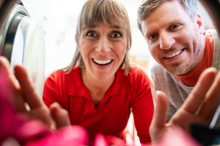 A man and a woman look cheerfully into an open washing machineの写真素材