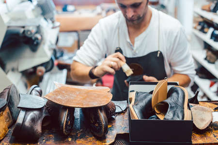 Shoemaker putting glue on sole of a shoe to fixの写真素材