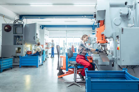 Woman worker in factory producing metal parts on punching machineの写真素材