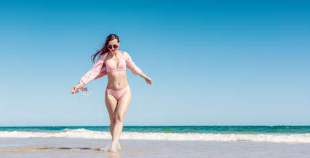 Woman having fun walking in the water on a sandy beach under a clear blue skyの写真素材
