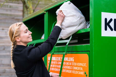 Young woman putting old or used clothes into donation binの写真素材
