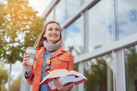 Woman student with books and coffee on university campus having a good dayの写真素材