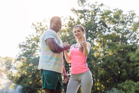 Fitness couple in summer park with woman giving thumbs-up to cameraの写真素材