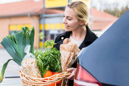 Woman storing basket with groceries into trunk after shopping