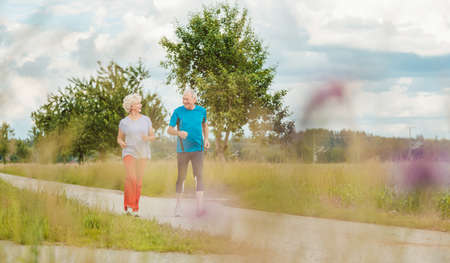 Fit and active senior couple running outdoors as exerciseの写真素材