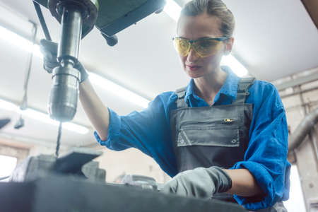 Woman worker in metal workshop using pedestal drill