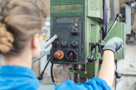 Woman worker in metal workshop operating power drillの写真素材