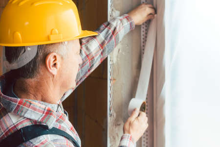 Male construction worker applying tape on wall