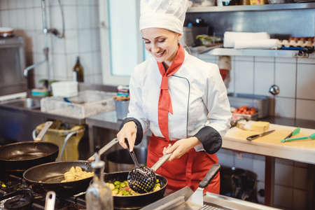 Woman chef with pans and pots preparing food in the restaurant kitchenの写真素材