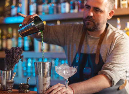 Barman gently pouring beer into shaker on bar counter