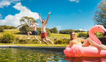 Friends jumping in water of public pool in summerの写真素材