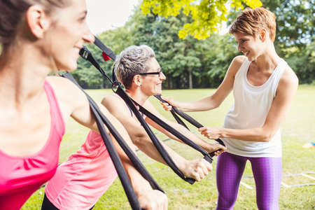 Happy mature athletic woman doing exercises with the female personal fitness trainer in the park