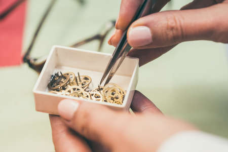Watchmaker sorting gears in little container with pincersの写真素材