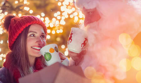 Santa Claus having mulled wine with woman on Christmas marketの写真素材