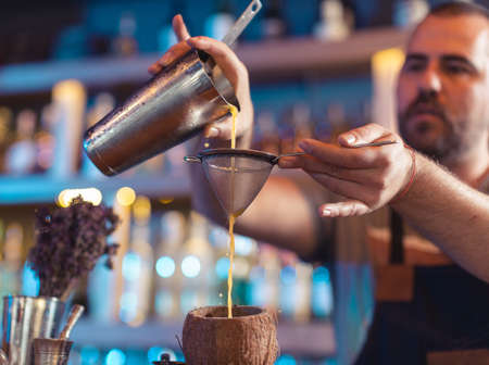 Bartender pouring juice using strainer in coconut shell in barの写真素材