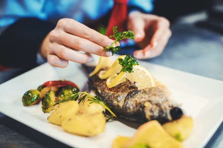 Chef cook in a fancy restaurant kitchen finishing a dish with careの写真素材
