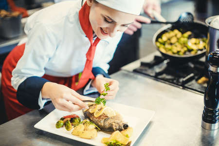 Chef cook in a fancy restaurant kitchen finishing a dish with careの写真素材