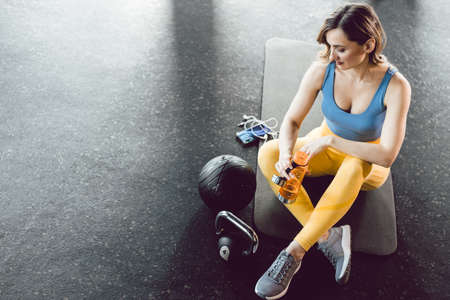 Beautiful young woman on gym floor drinking waterの写真素材