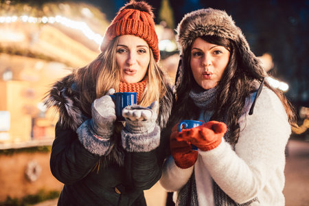 Two women with hot mulled wine in front of Christmas market standの写真素材