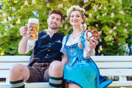 Couple in Bavaria sitting on bench toasting with beerの写真素材