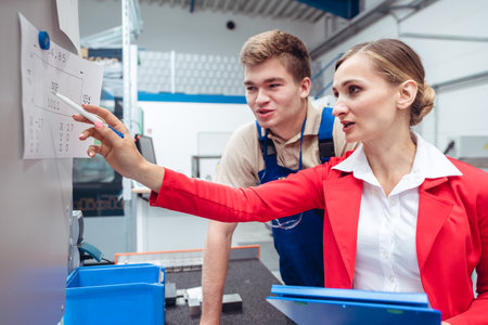 Worker and manager on factory floor discussing product specificationsの写真素材