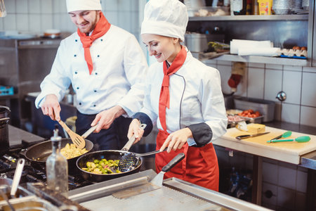 Chef woman and man cooking together in a restaurant kitchenの写真素材