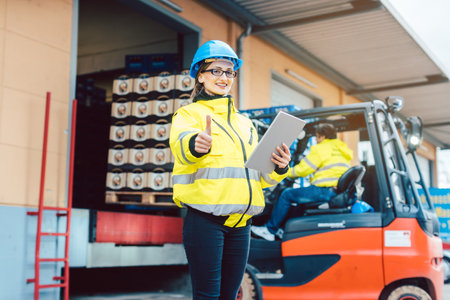 woman in front of forklift transporting goods from warehouseの写真素材