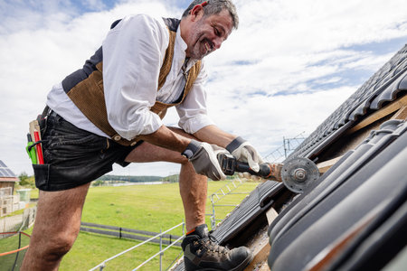 Roofer in traditional gear working on roof using sawの写真素材