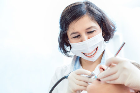 Female dentist wearing smiling face mask during a dental procedureの写真素材