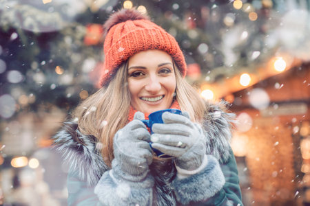 Woman in front of Christmas tree on winter market drinking hot wineの写真素材