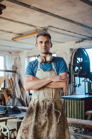 Carpenter standing in his wood workshop looking at cameraの写真素材